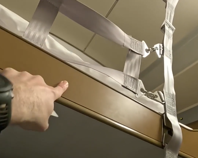 Stefano Mini indica il bordo di un letto con cinghie di sicurezza bianche e fibbie metalliche.