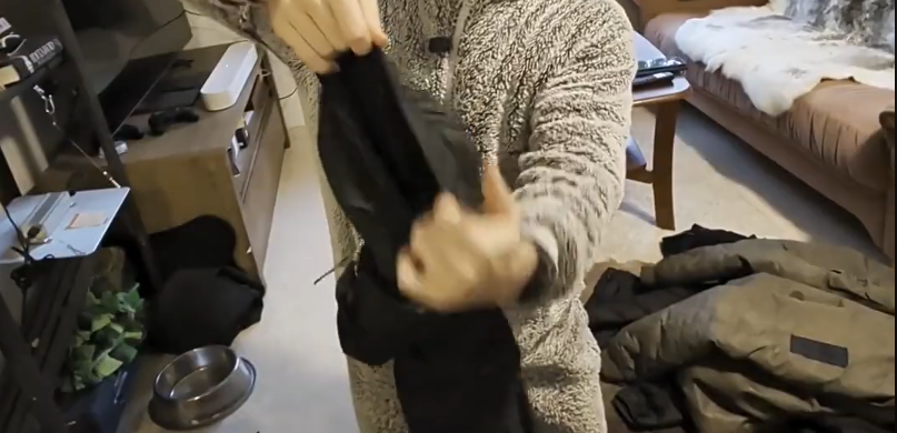 Una persona con un maglione soffice beige tiene in mano un capo di abbigliamento nero, mostrando l'interno, in una stanza con