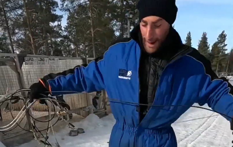 Stefano Mini in tuta da neve tiene in mano una linea da sleddog in un ambiente innevato.