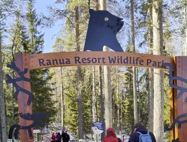 Ingresso al Ranua Resort Wildlife Park con un arco in legno e silhouette di animali, circondato da una foresta innevata.