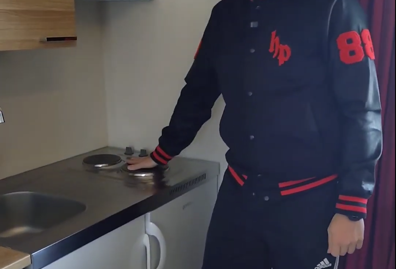 Stefano Mini in una piccola cucina con la mano su un fornello elettrico.