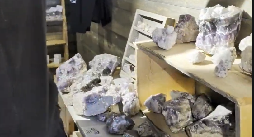 Vari cristalli grezzi di ametista e quarzo esposti su scaffali di legno in un negozio di minerali.