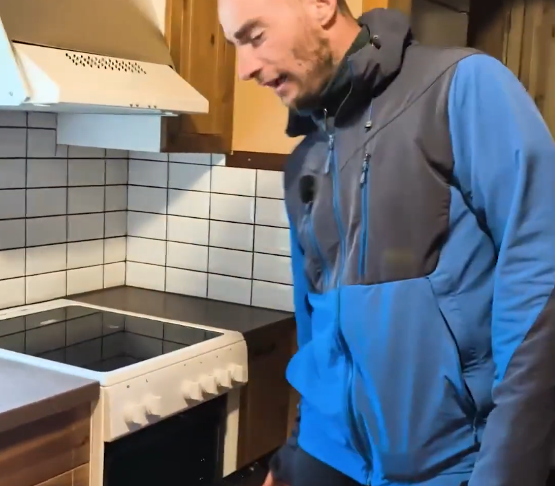 Stefano Mini in una cucina con piastrelle bianche, vicino a un fornello elettrico e una cappa.