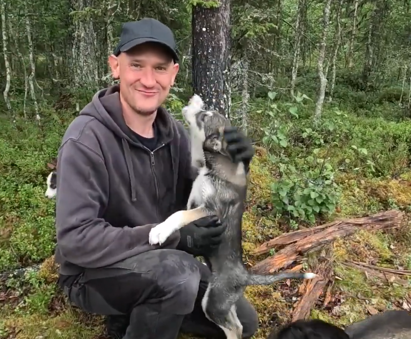 Raine Niemi sorride mentre tieni in braccio un cucciolo di husky in una foresta.
