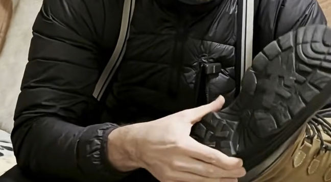 Stefano Mini mostra la suola antiscivolo di uno scarpone da trekking marrone, evidenziando il battistrada robusto.