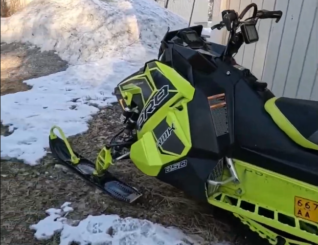 Motoslitta Polaris RMK 850 nera e giallo neon parcheggiata su terreno con neve e erba secca.