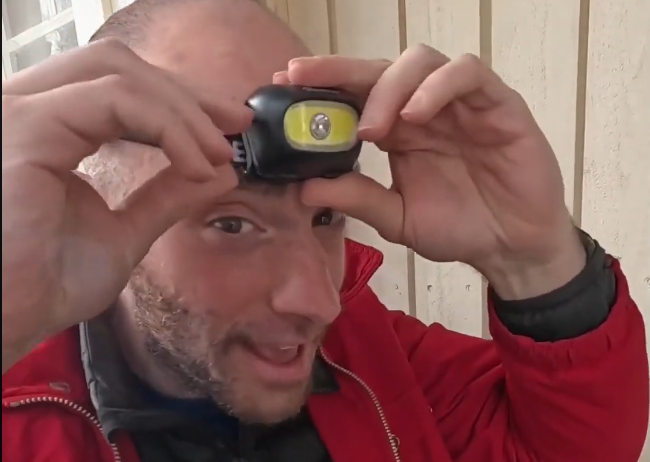 Stefano Mini regola una lampada frontale sulla sua fronte, con la luce gialla accesa, indossando una giacca rossa.