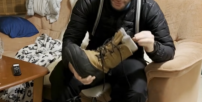 Stefano Mini esamina uno stivale da trekking marrone e nero mentre è seduto su un divano.