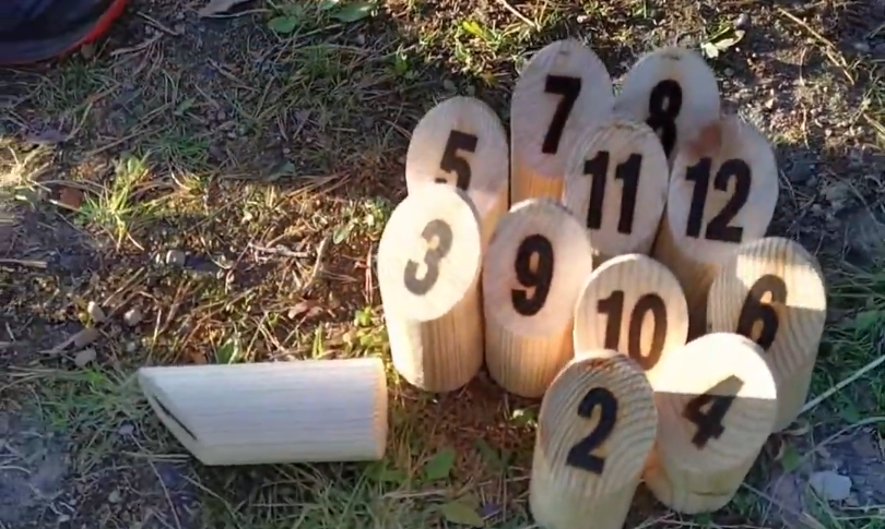 Set di birilli in legno numerati per il gioco del Mölkky, con un birillo da lancio a terra sull'erba.