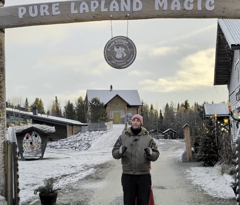 Stefano Mini sorride all'ingresso dell'Elves Village in Lapponia, sotto un arco di legno con la scritta "Pure Lapland Magic"