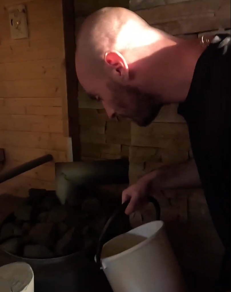 Stefano Mini versa acqua dentro a una sauna a legna.