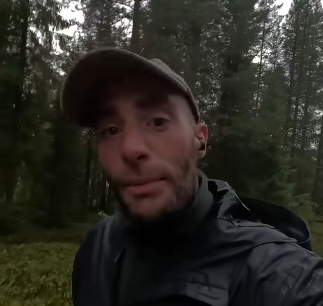 Stefano Mini in una foresta, indossa un cappello e una giacca scura, guardando la fotocamera.