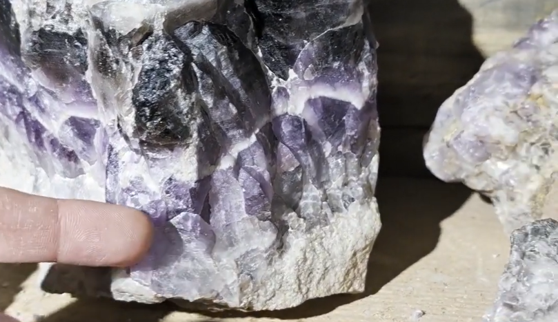 Stefano Mini indica una grande geode di ametista viola e bianca con cristalli scintillanti.