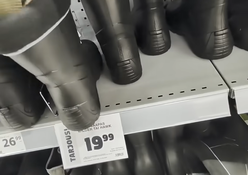 Stivali di gomma neri in esposizione su uno scaffale di un negozio, con un cartellino del prezzo che indica "SAAPAS WILDER TA