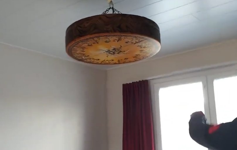 Lampada a soffitto rotonda decorata con motivi floreali, tende rosse e la mano di Stefano Mini che si estende verso una fines