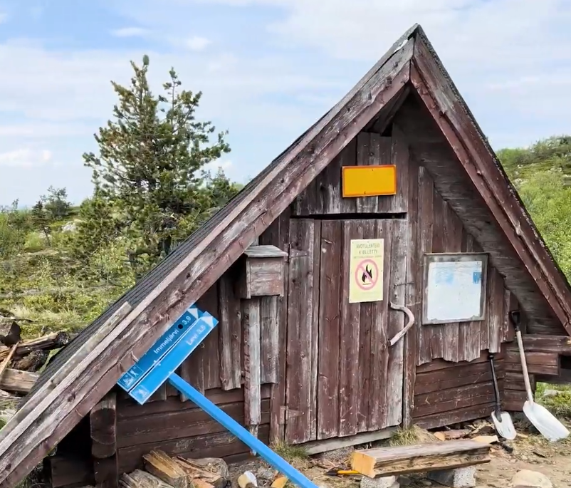 Capanna di legno rustica con tetto scuro in un paesaggio naturale. Segnaletica per Immeljärvi e divieto di fuochi aperti.