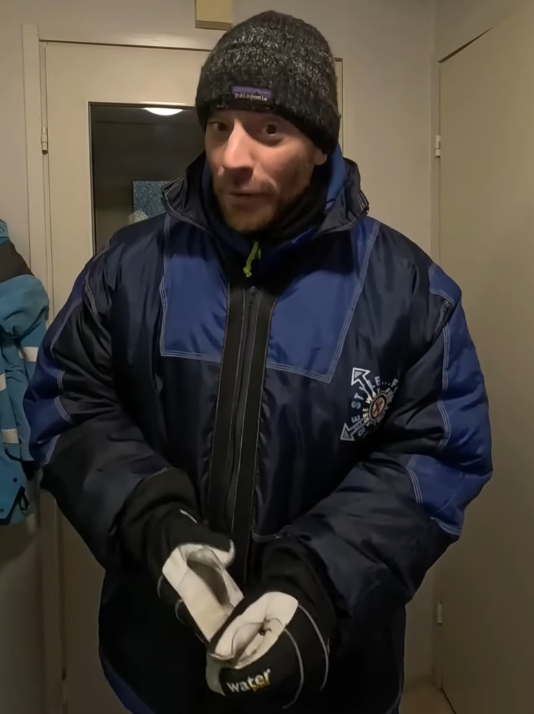 Stefano Mini indossa un berretto Patagonia, una giacca invernale blu e guanti, in piedi in un corridoio.