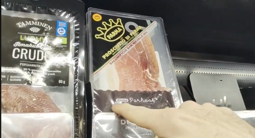 Stefano Mini indica una confezione di Prosciutto di Parma in un supermercato, con un'altra confezione di crudo sullo sfondo.