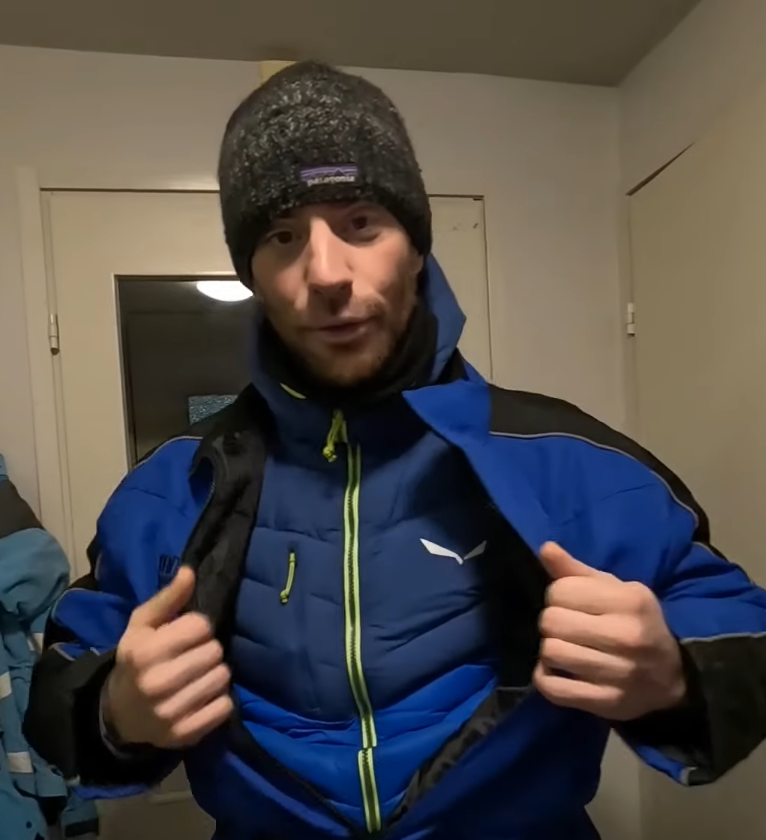 Stefano Mini indossa un berretto Patagonia e una giacca invernale blu e nera, mostrando una giacca piumino Salewa sottostante