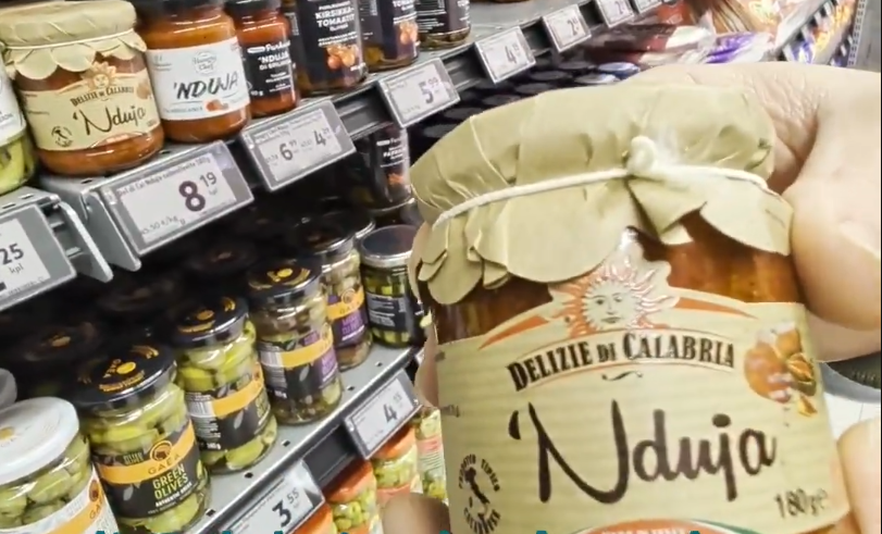 Mano che tiene un barattolo di 'Nduja Delizie di Calabria in un supermercato, con altri prodotti sugli scaffali.