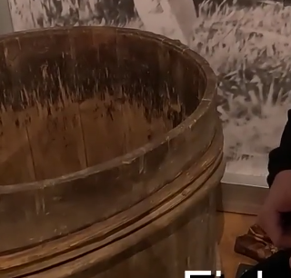 Dettaglio di un vecchio barile di legno rustico e consumato, con cerchi in metallo, esposto in un ambiente interno.