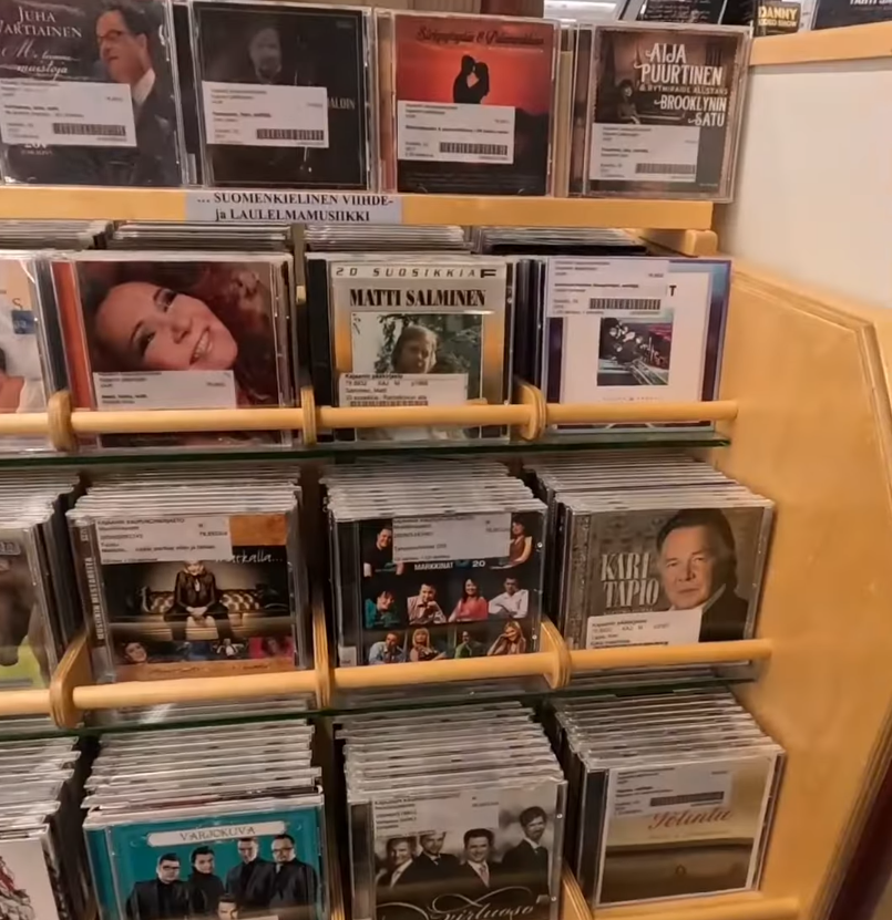 Scaffale di legno in un negozio, pieno di CD musicali finlandesi con copertine che mostrano vari artisti.