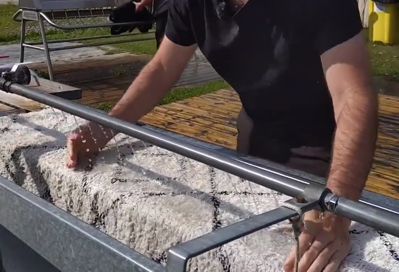 Stefano Mini lava a mano un grande tappeto bianco e nero in una vasca metallica all'aperto.