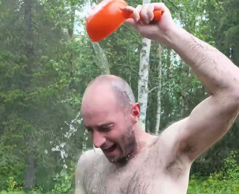 Stefano Mini si versa acqua fresca sulla testa con un mestolo arancione all'aperto, sorridendo.