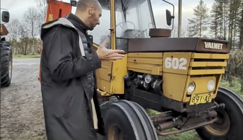 Stefano Mini mostra un trattore Valmet 602 giallo con targa 891-AO in un ambiente rurale.