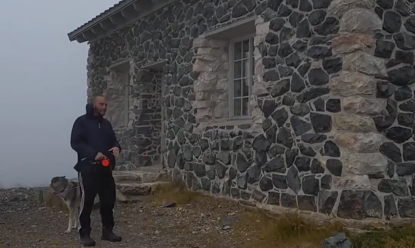 Stefano Mini e il suo cane davanti a un rifugio in pietra in una giornata nebbiosa.
