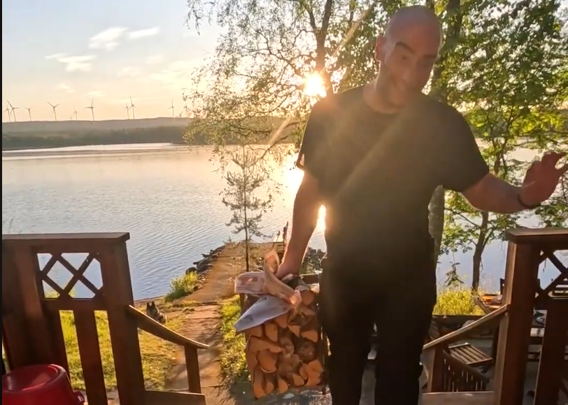 Stefano Mini porta legna da ardere al tramonto con un lago e turbine eoliche sullo sfondo.