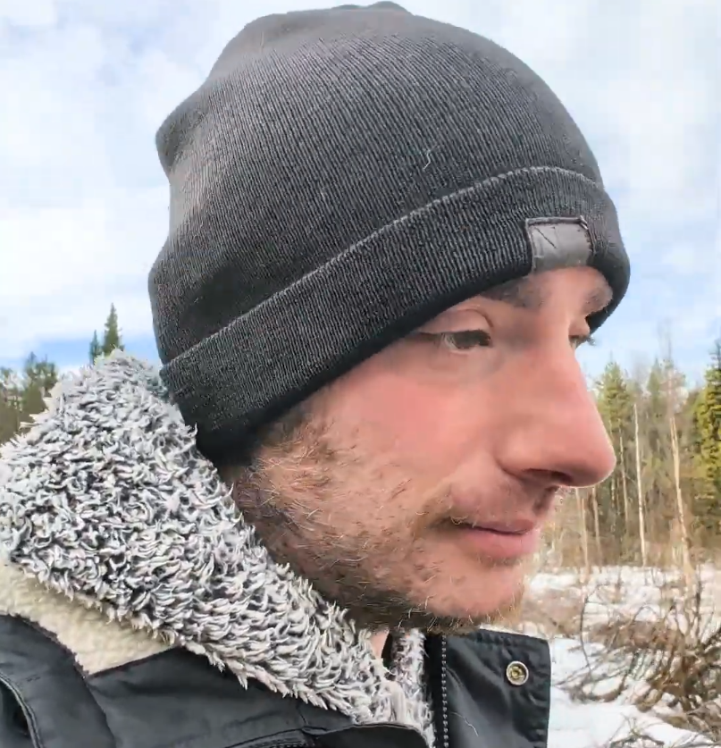 Stefano Mini con berretto scuro e giacca invernale, all'aperto in un paesaggio innevato con alberi.