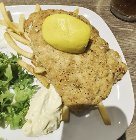Piatto contenente una cotoletta, limone, patatine fritte, insalata e salsa bernese.