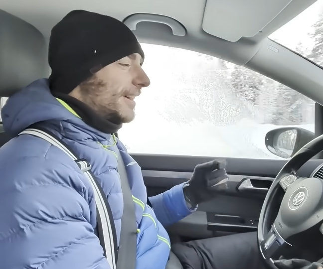 Stefano Mini in auto con giacca blu e berretto nero, sorride mentre guida su strada innevata.