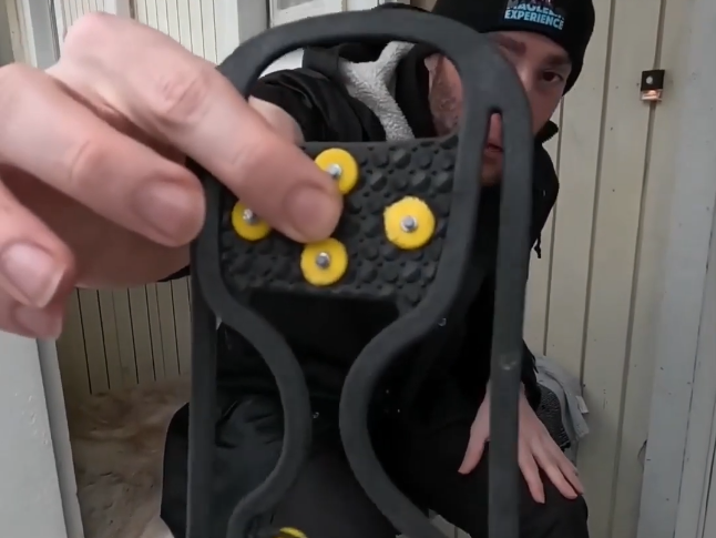 Stefano Mini mostra un dispositivo antiscivolo nero con tacchetti gialli per scarpe, utile per camminare su neve e ghiaccio.