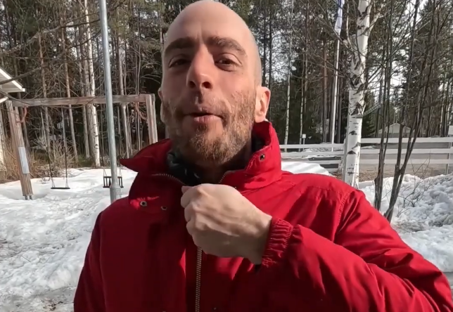 Stefano Mini con giacca rossa in un paesaggio innevato con alberi e altalene sullo sfondo.