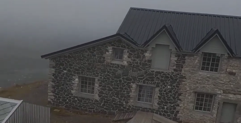 Casa in pietra con tetto scuro sotto un cielo grigio e nuvoloso, in un paesaggio desolato.