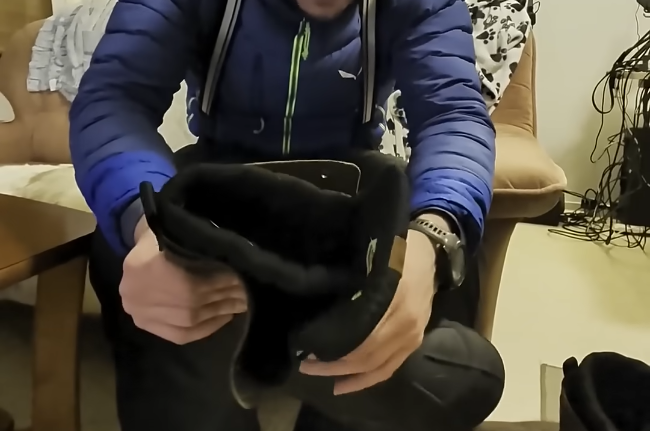 Stefano Mini tiene in mano uno scarpone nero, indossando una giacca blu e pantaloni neri.