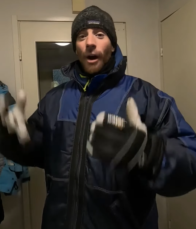 Stefano Mini con giacca invernale blu e nera, berretto e guanti, con espressione sorpresa e mani alzate.