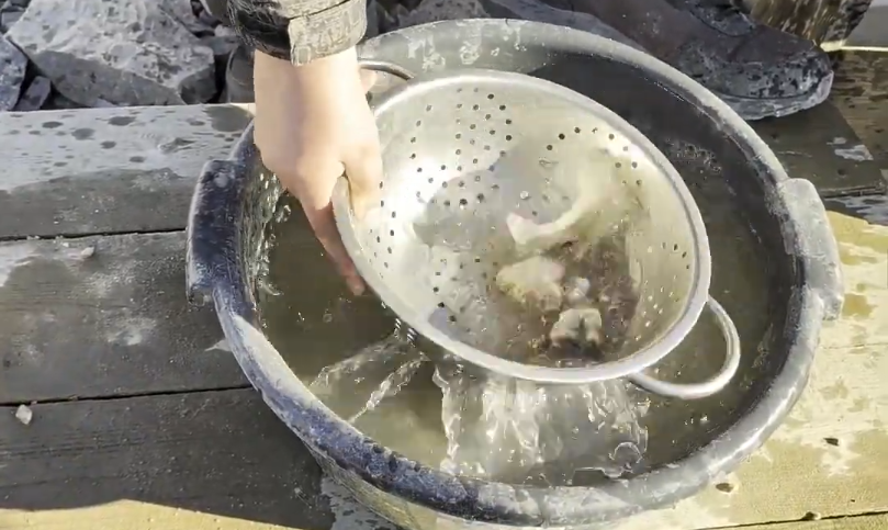 Mano che lava pietre in un colino dentro un secchio d'acqua, con l'acqua che scorre via dai fori.