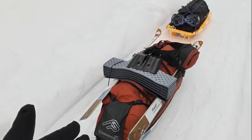 Due pulka cariche di attrezzatura da sci su neve fresca, con una mano guantata che le trascina in una spedizione invernale.