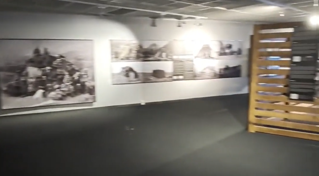 Sala espositiva con fotografie in bianco e nero appese alle pareti e un espositore in legno sulla destra.