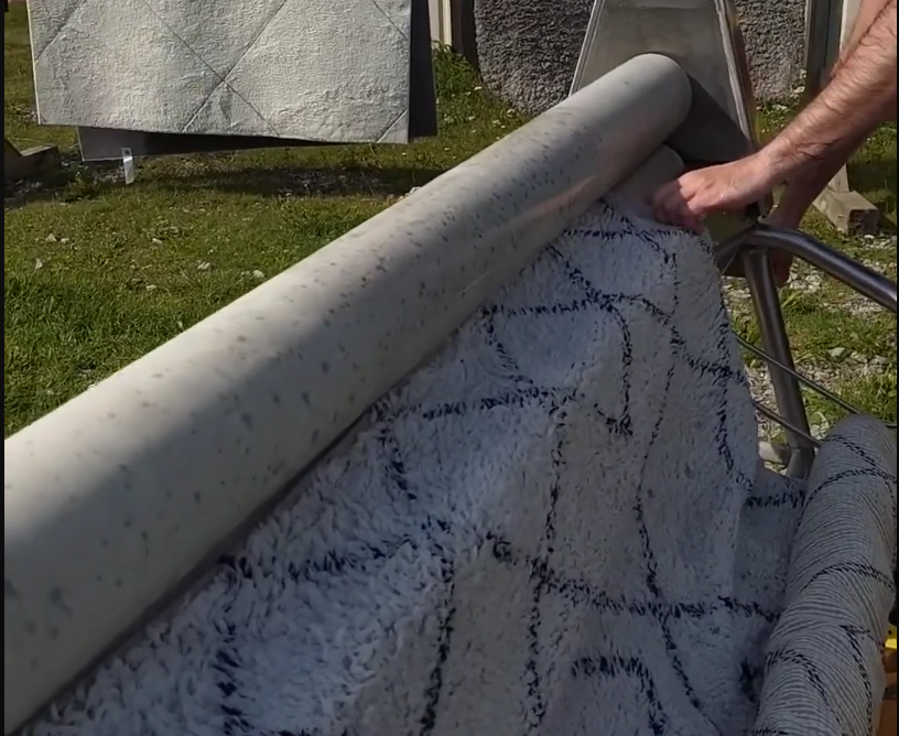 Stefano Mini alimenta un tappeto bianco e nero con motivo geometrico in una macchina a rulli per la pulizia e l'asciugatura.