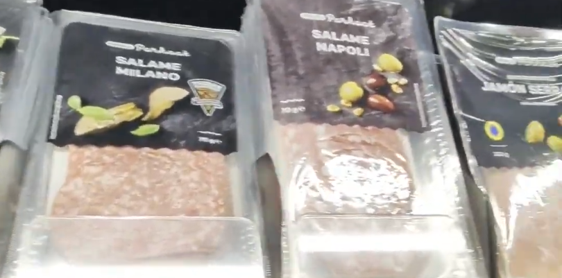 Confezioni di salame Milano, salame Napoli e jamón serrano affettati, esposti in un banco frigo di un supermercato.