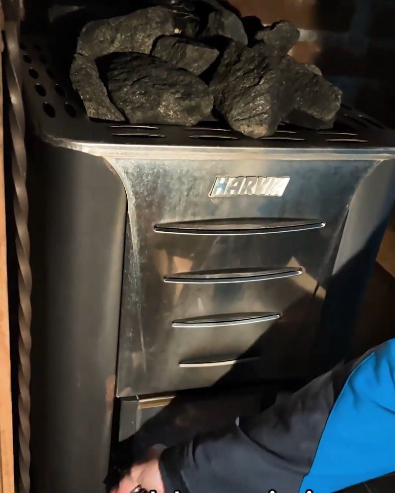 Riscaldatore per sauna Harvia con pietre vulcaniche in cima. Una mano sta regolando i comandi del riscaldatore.